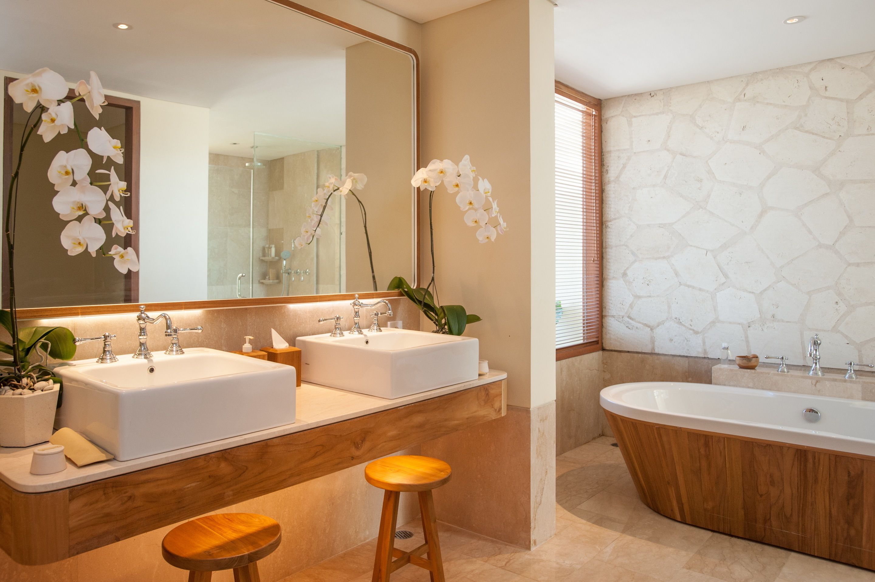 Een moderne badkamer met twee wastafels, een ruime badkuip en een houten krukje.