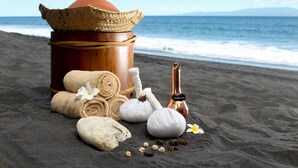 A beach setting with a large clay pot, rolled towels, a bottle, and some stones on the sand. - Komaneka at Keramas Beach (Gianyar)