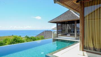 A modern infinity pool with a clear view of the ocean, a covered seating area, and a large window with curtains.