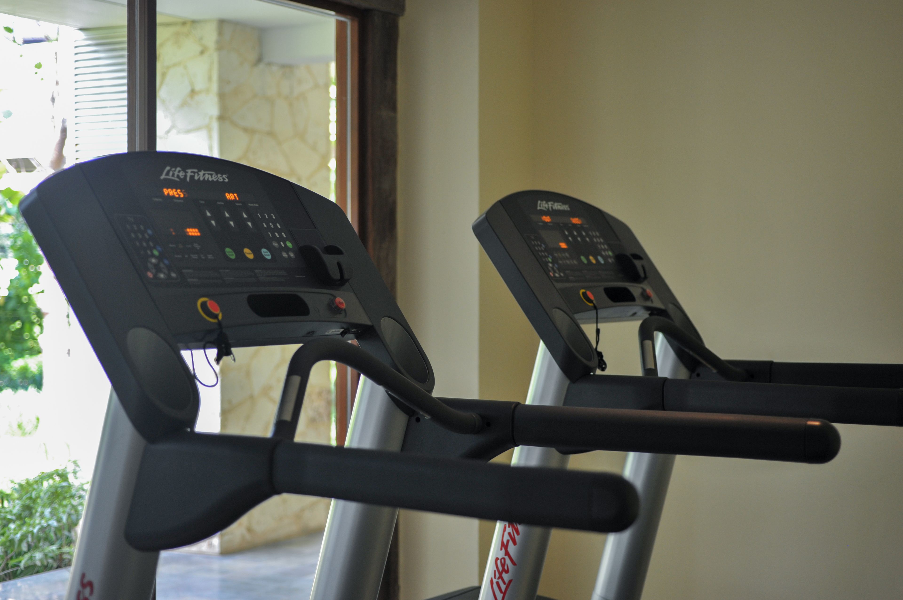 Two Life Fitness treadmills in a room with a stone wall and a window.