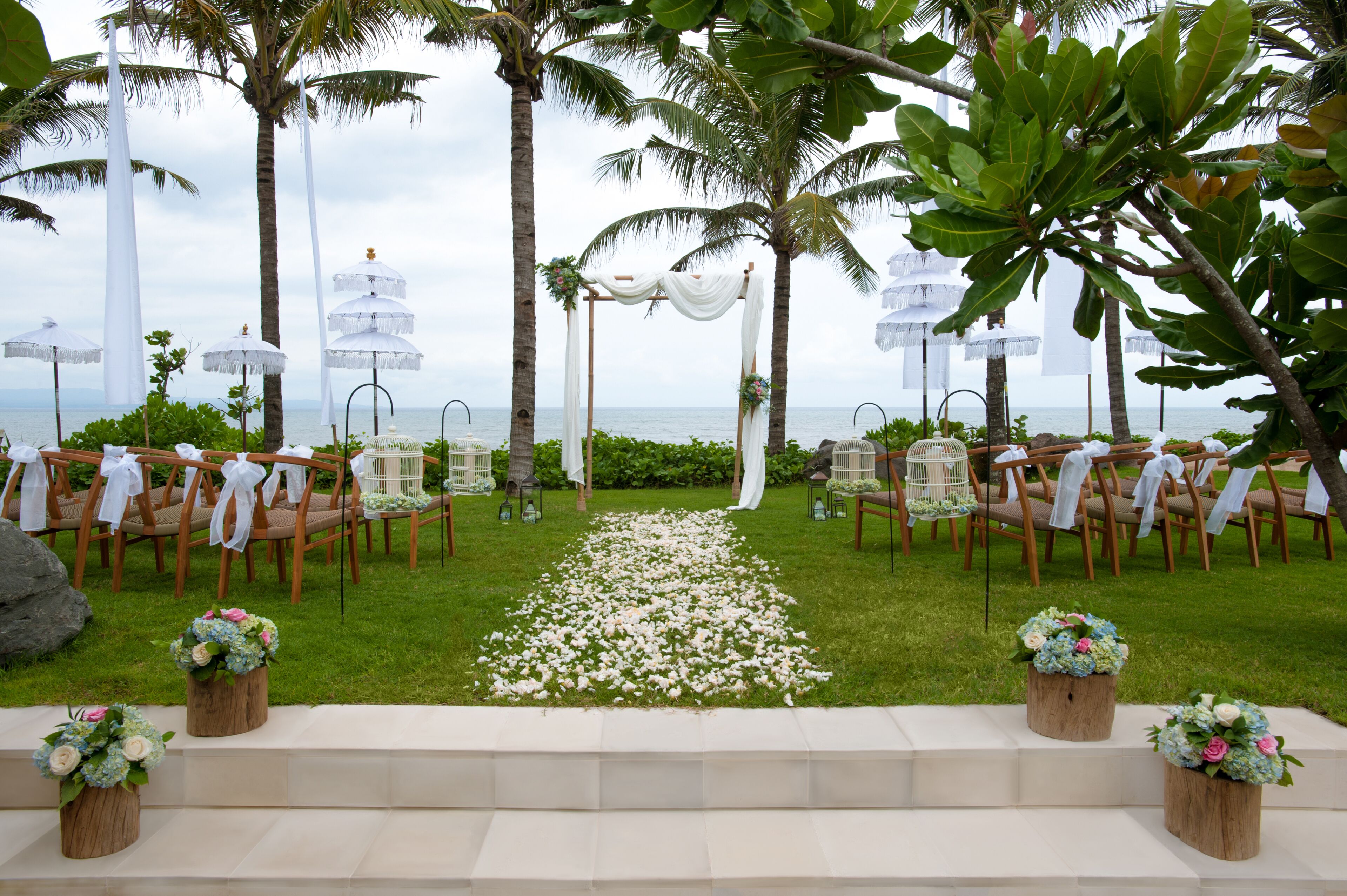 An outdoor wedding ceremony setup with chairs arranged in rows, a white aisle, and flower arrangements on wooden stands.