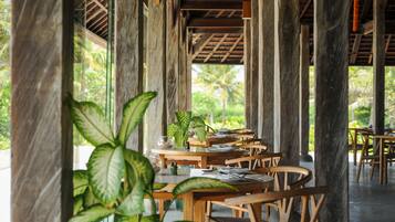 An outdoor wooden pavilion with tables and chairs, surrounded by lush greenery.