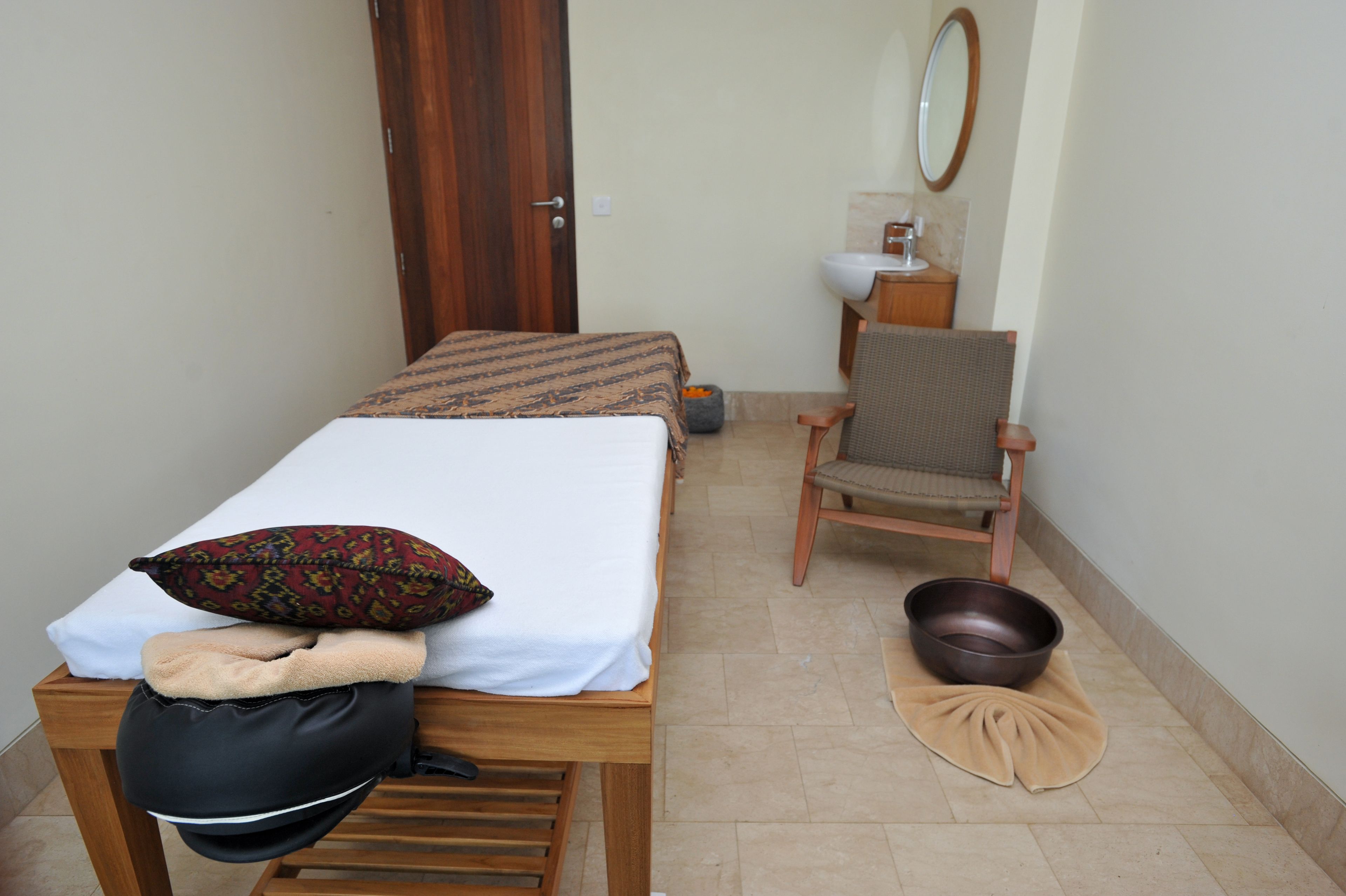 A small, neatly arranged bedroom with a single bed, a chair, a sink, and a mirror.