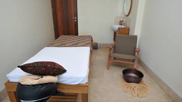 A small, neatly arranged bedroom with a single bed, a chair, a sink, and a mirror.