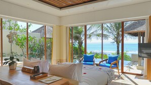 A hotel room with a large bed, a desk with a computer and a plant, a TV, and a view of the ocean. - Komaneka at Keramas Beach (Gianyar)