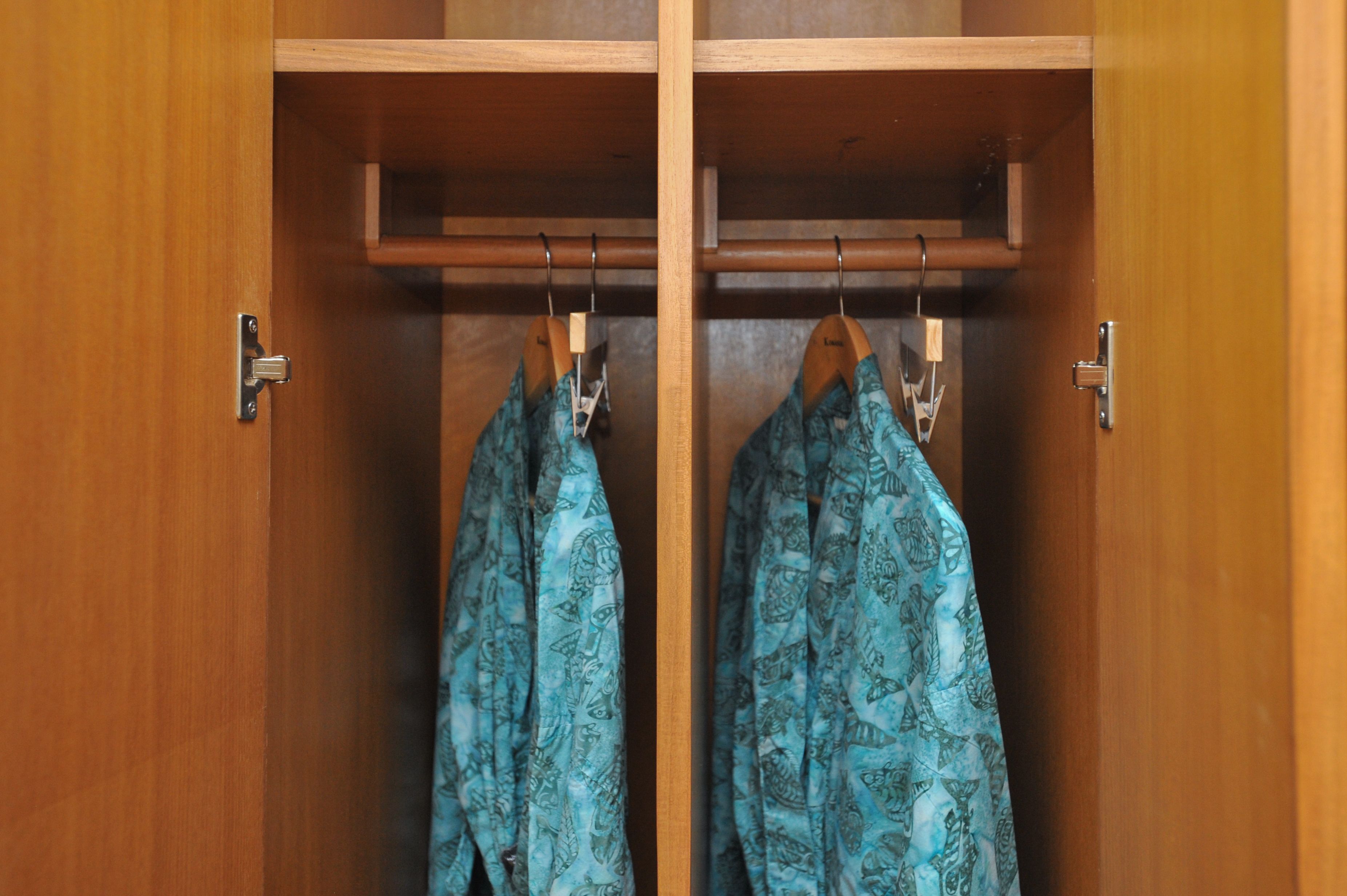 A wooden wardrobe with two hangers holding patterned garments.