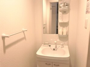 A bathroom with a white sink, a mirror, a towel rack, and a shelf with toiletries. - At RLiS House Tennoji East (Osaka)