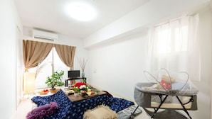A living room with a sofa, a dining table with a TV, a baby rocker, and a window with curtains.
