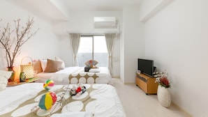 A hotel room with two beds, a TV, a dresser, and a window with curtains.