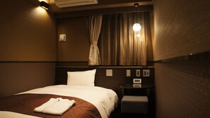 Habitación de hotel con cama, mesita de noche, reloj digital y ventana con cortinas.