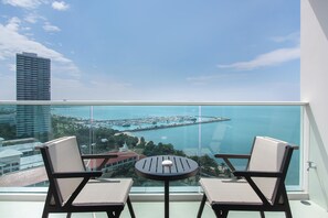 A balcony with two wicker chairs and a small round table, overlooking a marina and a coastal cityscape. - White Sand Beach Residences Pattaya (Sattahip)