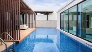 A modern indoor swimming pool with a wooden deck and a glass wall on one side. - White Sand Beach Residences Pattaya (Sattahip)