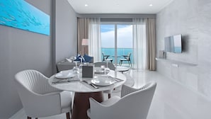 A modern hotel room with a dining area, a TV mounted on the wall, and a view of the sea through large windows. - White Sand Beach Residences Pattaya (Sattahip)
