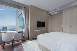 A modern hotel room with a large bed, a desk with a laptop, a TV mounted on the wall, and a view of the ocean. - White Sand Beach Residences Pattaya (Sattahip)