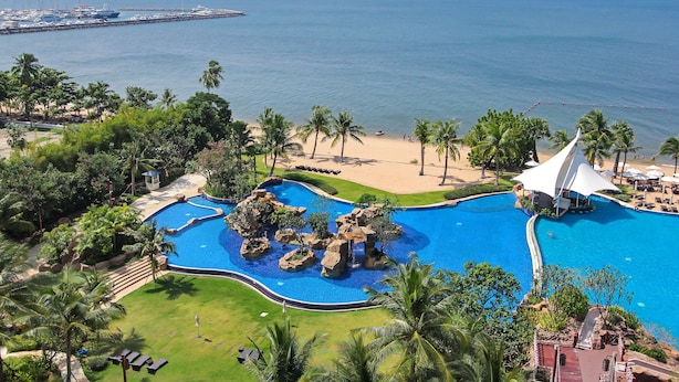 A resort with a large swimming pool, palm trees, and a view of the ocean. - White Sand Beach Residences Pattaya (Sattahip)