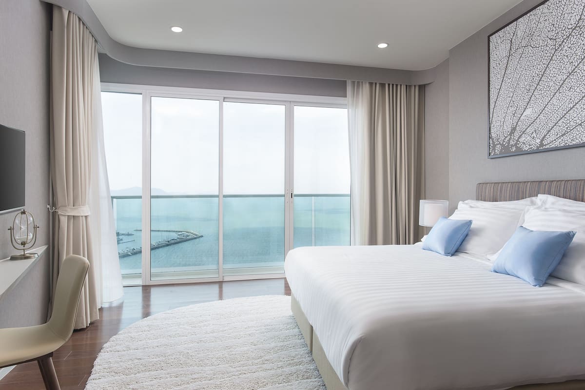 Ein Hotelzimmer mit einem großen Bett, einem Schreibtisch und Meerblick durch raumhohe Fenster.