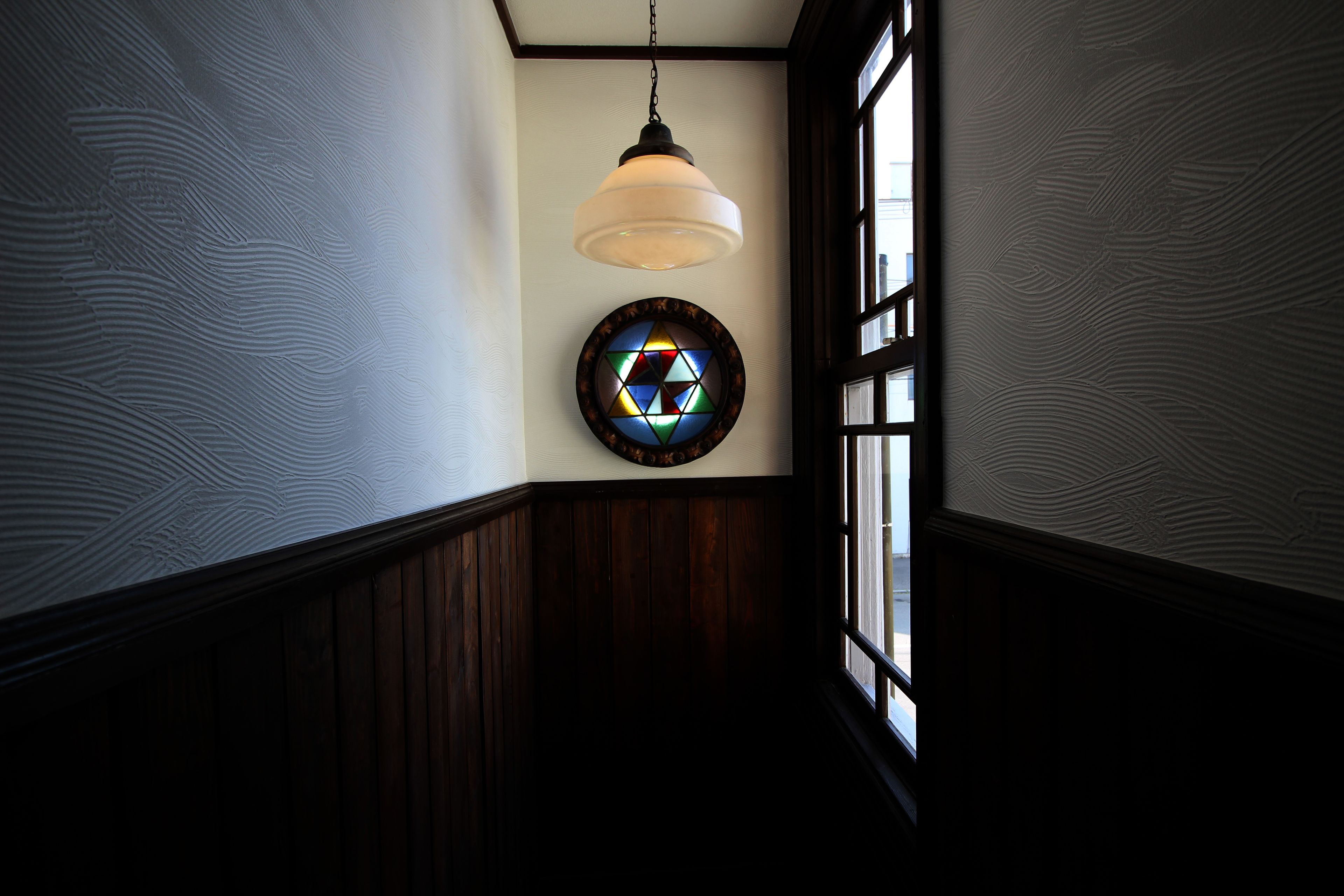 A hallway with a wooden wainscoting, a hanging pendant light, and a stained glass window.