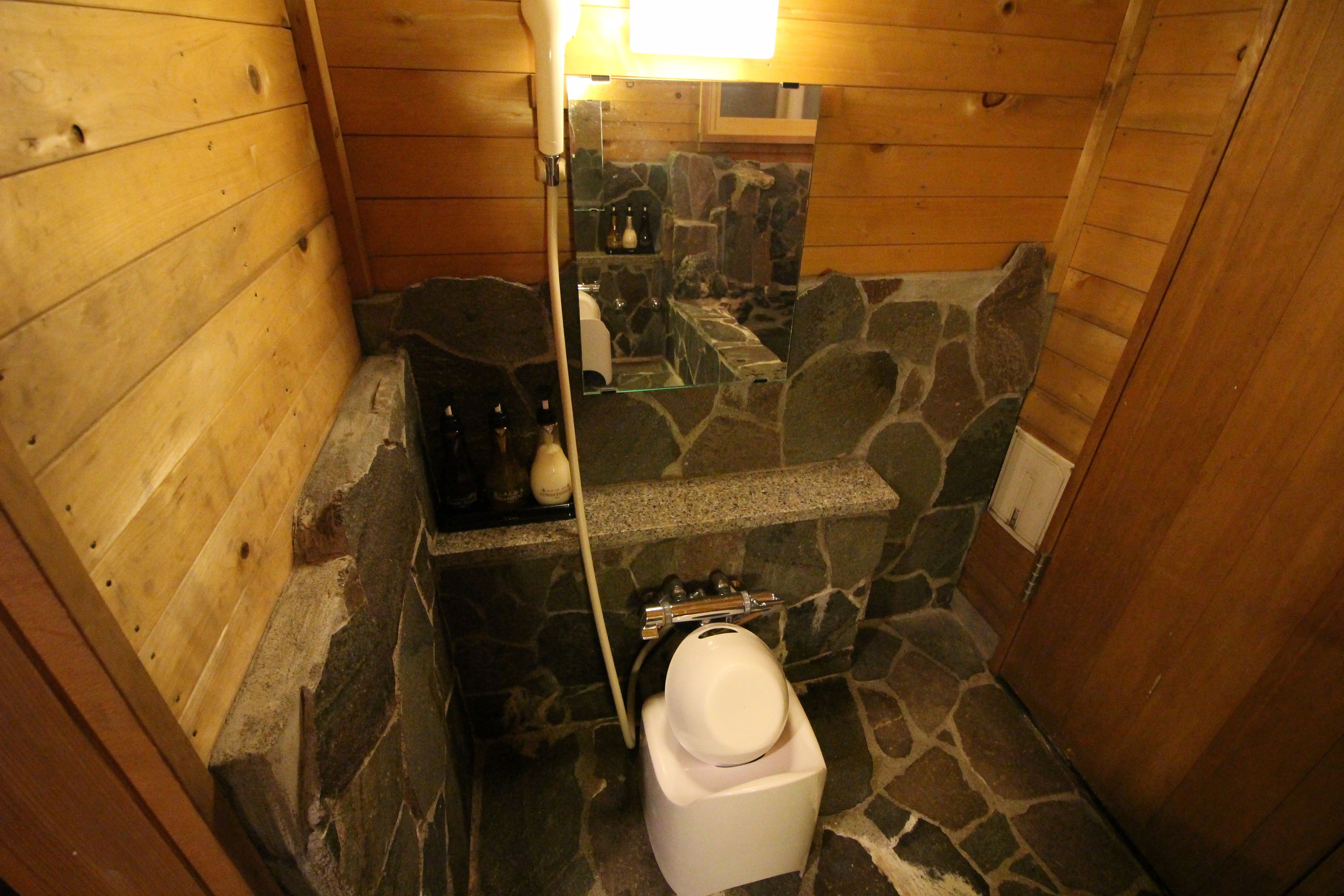 A small, wooden cabin-style bathroom with a stone shower area and a white toilet.