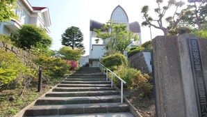 A set of stone steps leading up to a building with a pointed roof, surrounded by greenery and a stone wall. - Hakodate Classic Hotels (Hakodate)