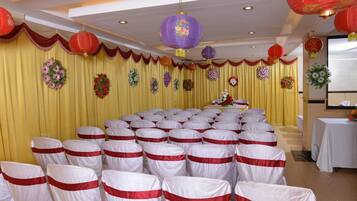 Un salón de banquetes con filas de sillas cubiertas con lazos blancos y rojos, cortinas amarillas y faroles rojos y morados.