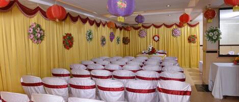 A banquet hall with rows of chairs covered in white and red sashes, yellow curtains, and red and purple lanterns.