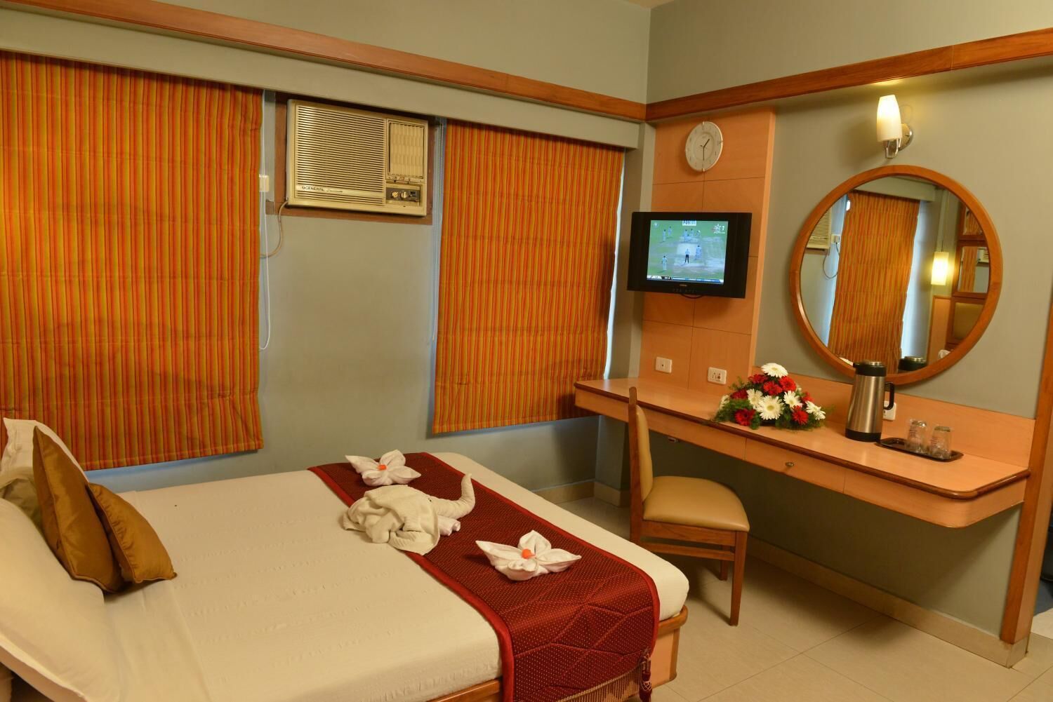 Una habitación de hotel con cama, escritorio, silla, televisor y espejo.