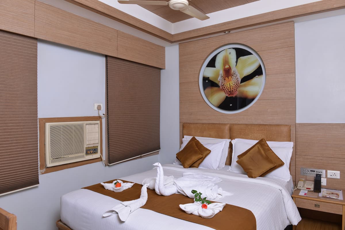 A hotel room with a bed, a round wall clock, a wall-mounted air conditioner, and a telephone on the nightstand.