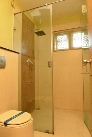 Un baño con cabina de ducha de vidrio, inodoro y ventana con celosías decorativas.