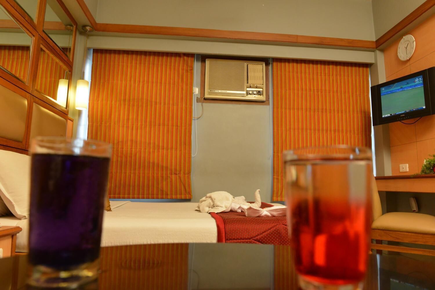 A compact room with a bed, a television, and a window with curtains.