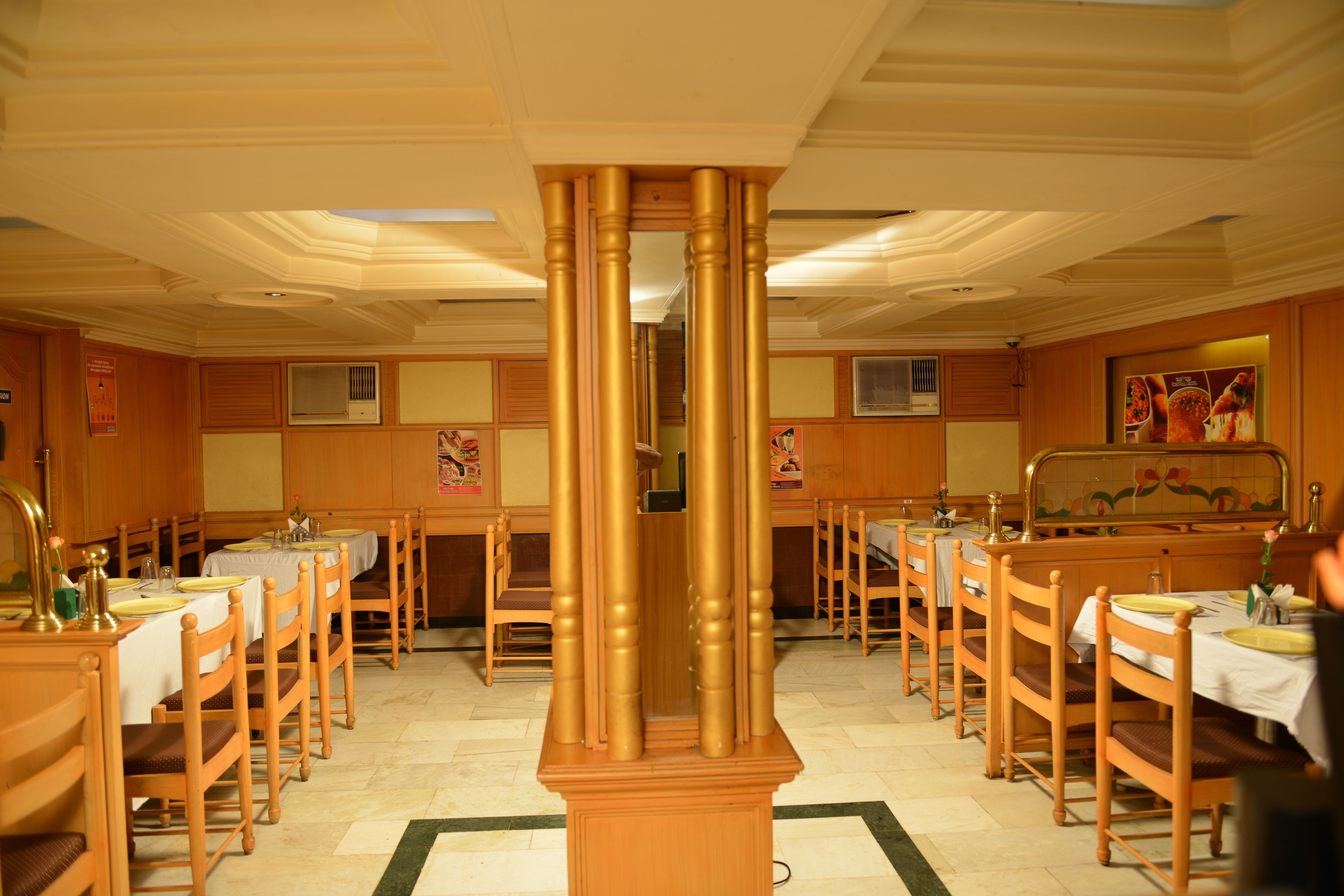 A dining area with wooden tables and chairs, a central decorative column, and a tiled floor.