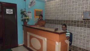 A reception desk with a wooden counter, a potted plant, and a wall with a patterned design. - Hotel Palms (Navi Mumbai)
