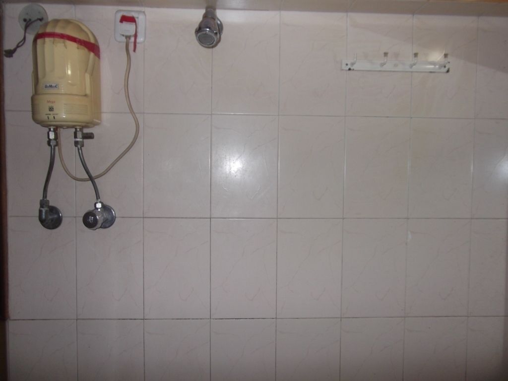 A bathroom with a shower head, a wall-mounted heater, and a power outlet.