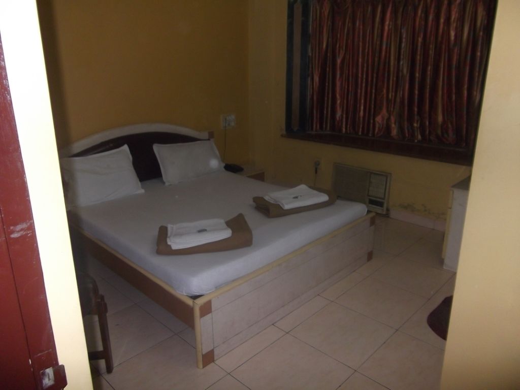 A single-bed room with a wooden frame, white bedding, and a window with curtains.