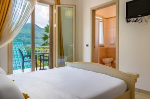 A hotel room with a bed, a balcony with a view of mountains, and a bathroom visible through an open door.