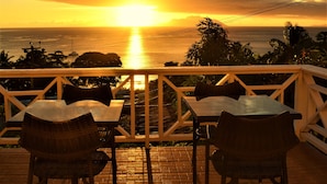 A sunset view from a terrace with tables and chairs, overlooking the ocean.