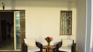 A room with two wicker chairs, a small table with a vase of flowers, a sliding glass door, and a window with decorative bars.