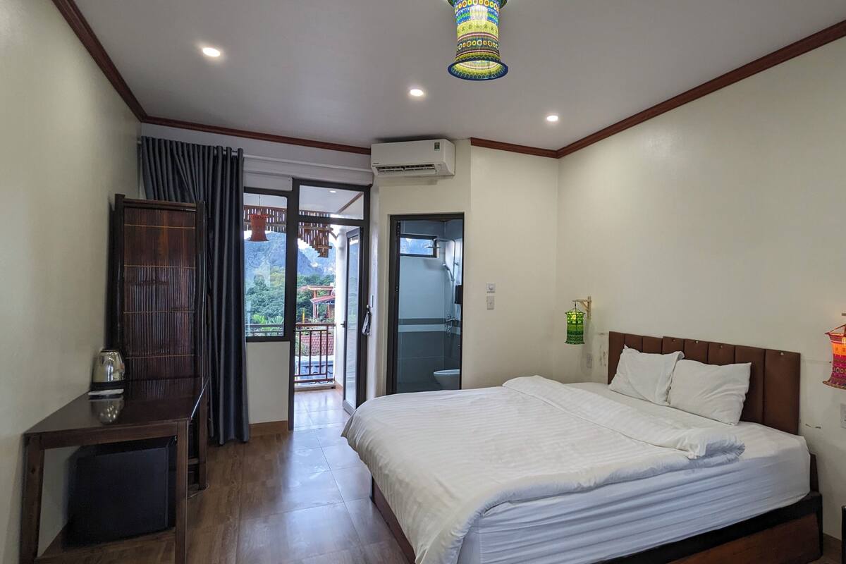 Une chambre d’hôtel équipée d’un lit, d’un bureau, d’un appareil de climatisation, d’un balcon avec vue et d’une applique murale décorative.