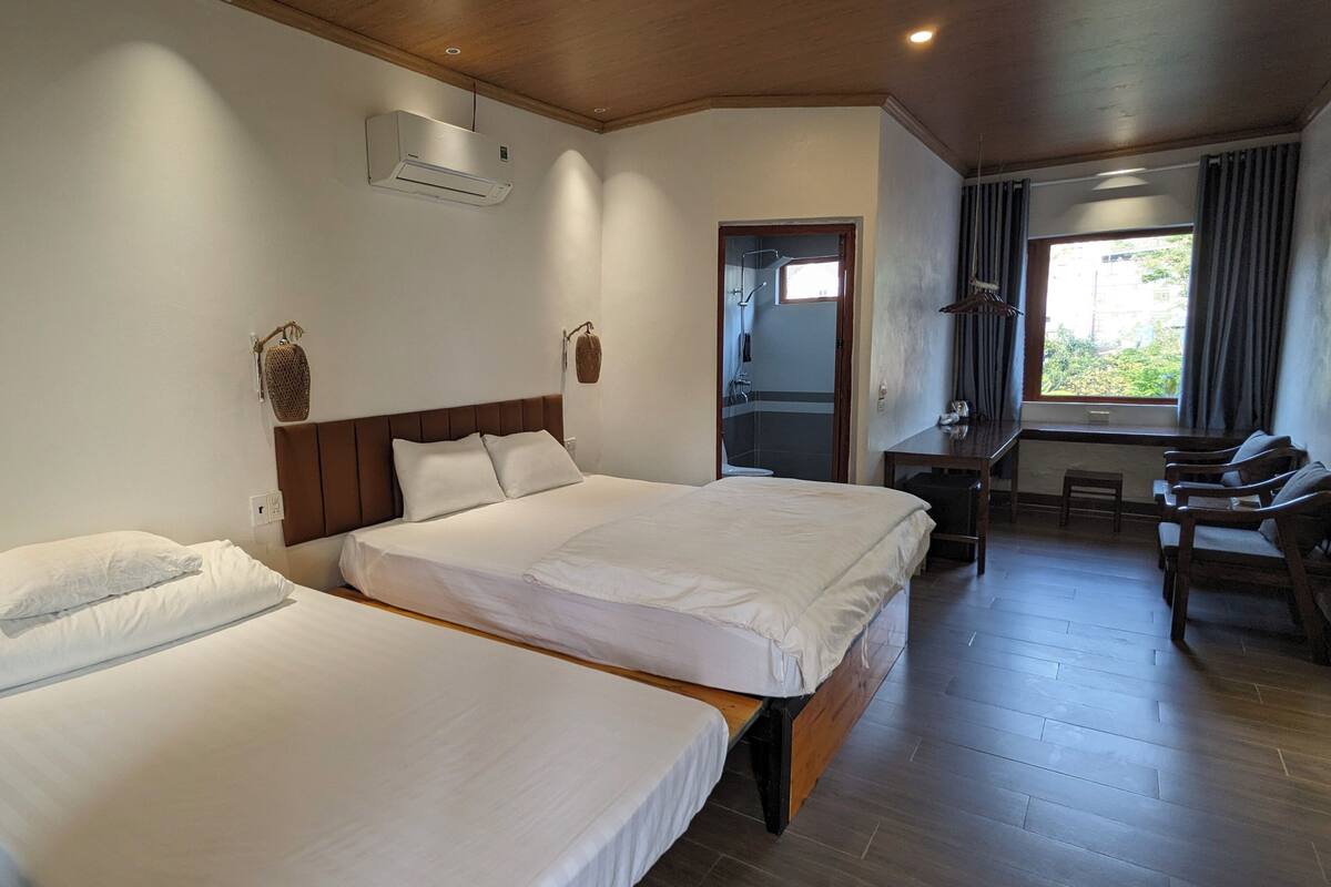 Une chambre d’hôtel avec deux lits, un bureau, une chaise, une fenêtre avec des rideaux et un appareil de climatisation.