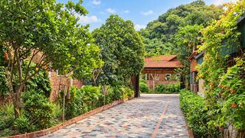 A paved pathway leading to a building with a red-tiled roof, surrounded by lush greenery and a brick wall.