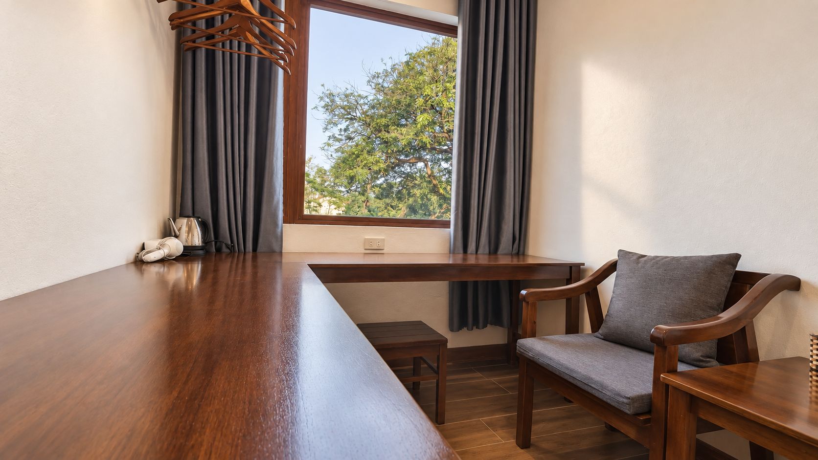 A room with a long wooden table, two chairs, a small table, and a window with curtains.