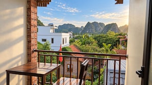 A balcony with a view of a mountainous landscape, a white building, and a red flag.