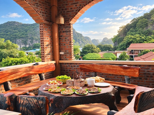 Une terrasse avec un mur en briques, des meubles en bois et une table dressée avec de la nourriture.