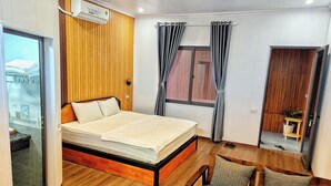 Un dormitorio con estructura de cama de madera, una mesita de noche, una silla, una ventana con cortinas y una puerta que da a otra habitación.