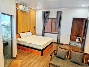 Ein Schlafzimmer mit einem hölzernen Bettgestell, einem Nachttisch, einem Stuhl, einem Fenster mit Vorhängen und einer Tür zu einem anderen Raum.