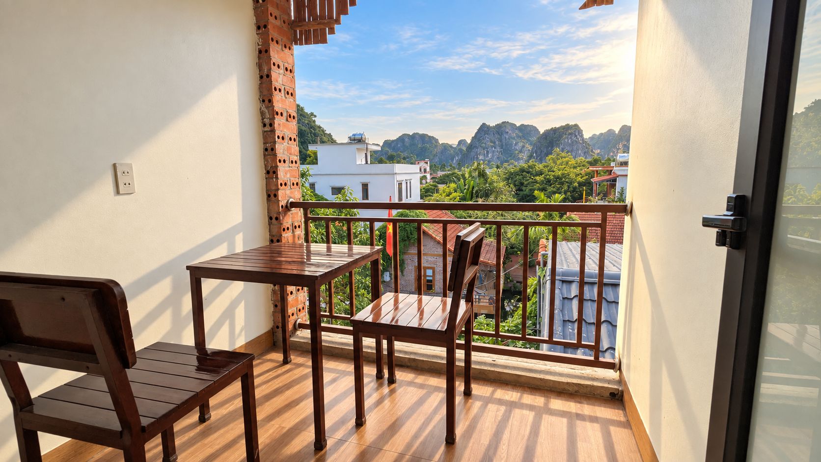 A balcony with a wooden table and chairs, a brick wall, and a view of buildings and mountains.