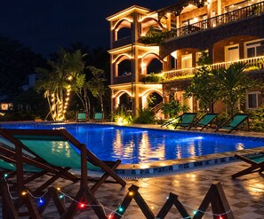 Ein Swimmingpool mit Liegestühlen und Lichterketten, umgeben von einem Gebäude mit mehreren Balkonen und Bögen.