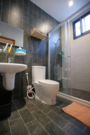 A modern bathroom with a toilet, sink, and glass shower enclosure. - Enjoy Home Stay (Tainan)