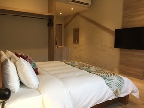 A modern bedroom with a large bed, a flat-screen TV mounted on the wall, and a small shelf with a decorative item. - Enjoy Home Stay (Tainan)