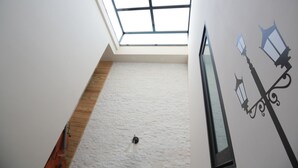Teto alto com claraboia, piso de madeira e luminária fixada na parede.