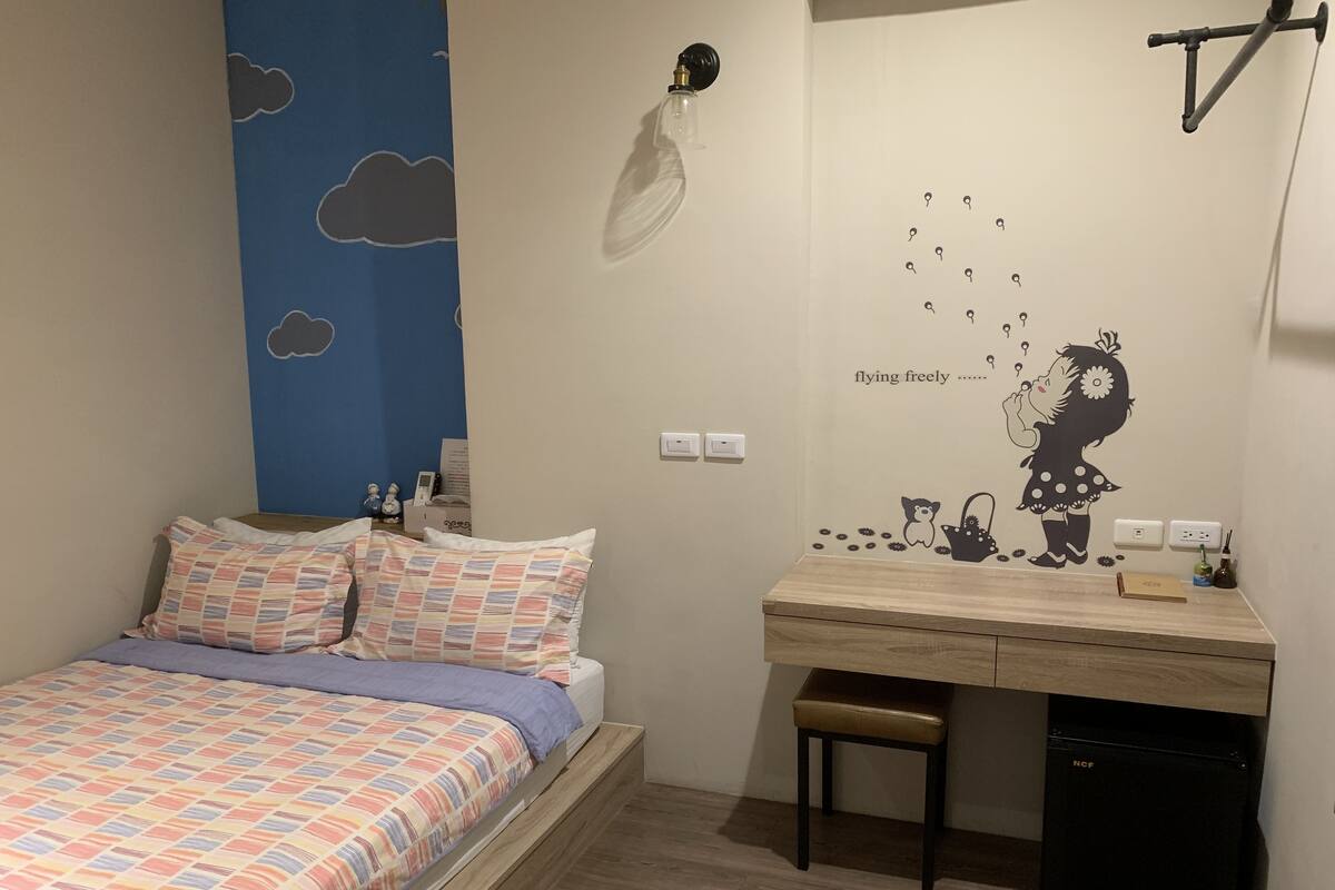 A bedroom with a bed, a desk, a chair, and a wall decal.